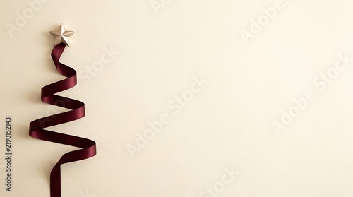 Minimalist abstract christmas tree shape made from a burgundy ribbon with a star topper