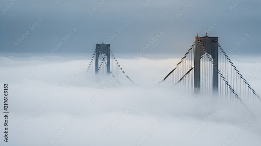 Obraz premium Suspension bridge towers rising above a thick layer of morning fog with a minimalist sky background