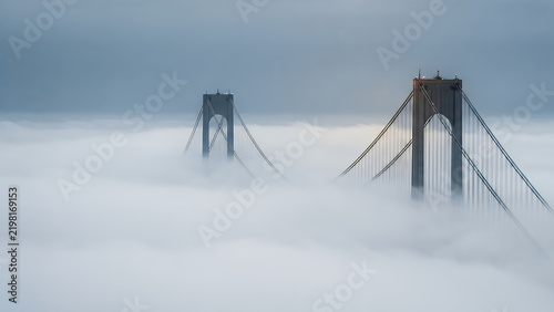 Suspension bridge towers rising above a thick layer of morning fog with a minimalist sky background