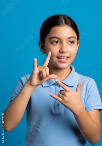 Young girl in light blue shirt signing on a bright blue background.