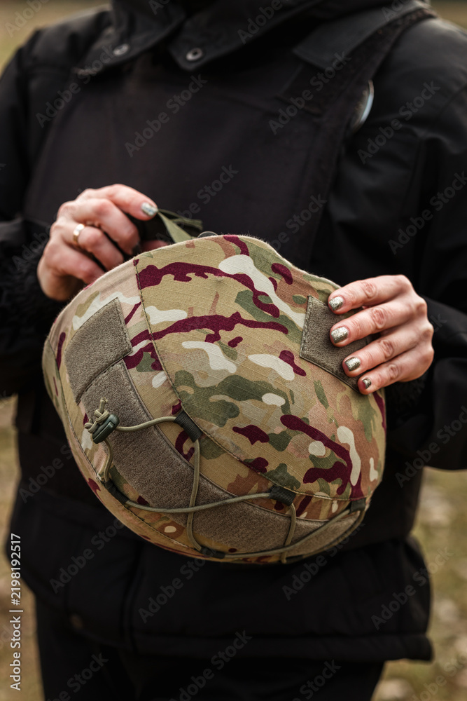 Obraz premium Woman holding military camouflage helmet in tactical vest