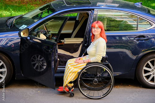 A young woman in a wheelchair next to her car.