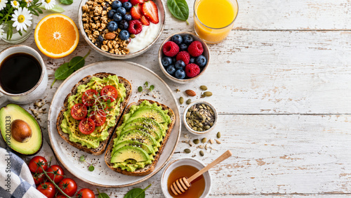 Healthy breakfast flat lay with avocado toast, berries, yogurt and fresh fruit on white wooden table