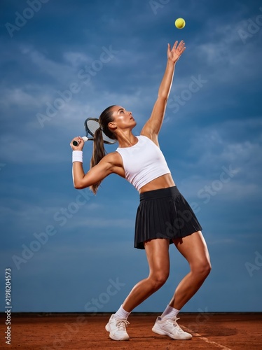 Female Tennis Player Serving on a Clay Court During a Match with a Dramatic Sky.