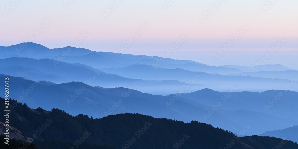 Naklejka premium Blue mountain ridges layered with pink sunrise sky