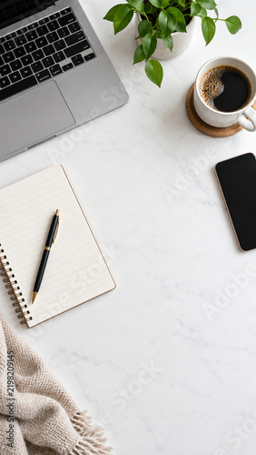 Minimal workspace flat lay with laptop, notebook, smartphone, coffee and green plant with copy space