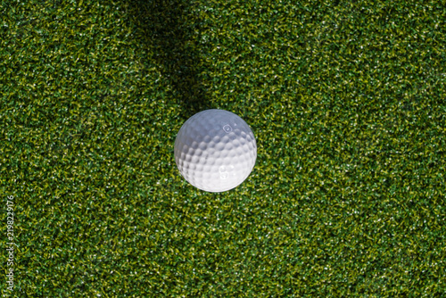White golf ball resting on vibrant green artificial turf, top-down view for sports equipment or leisure lifestyle branding