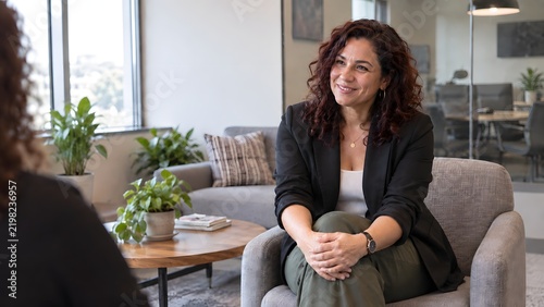 Portrait of confident businesswoman smiles at camera while attending job interview in modern office. Folded hands calm, gaze warming to the speaker, close up, soft light.