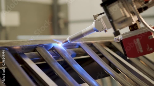 Automated CNC welding machine process, where a robotic nozzle joins metal tubes with a bright blue glow from the welding arc. Industrial metalworking, automation, and high-precision fabrication of ste