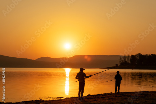 Father Son Fishing Together Lake Shore Sunrise Silhouette Casting Rod Active Hobby Parenting Outdoor Family Vacation Mountains Backdrop Golden Hour Natural Panorama Stock Photo
