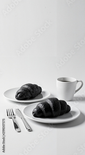 Black croissants and coffee on white plates with cutlery setting  