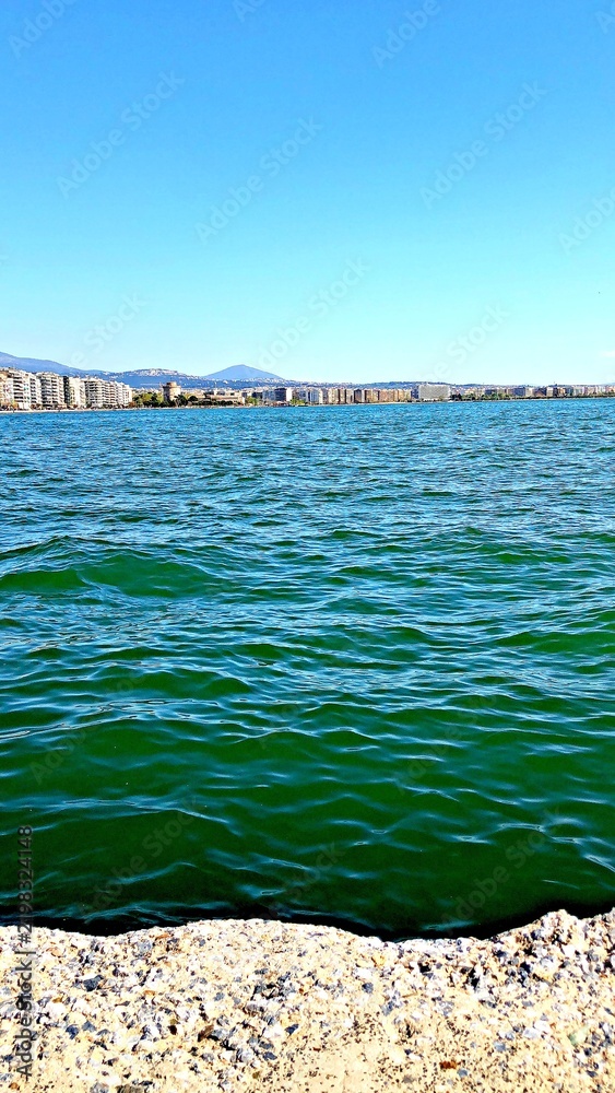 Fototapeta premium Ocean waves in front of a city skyline and blue sky