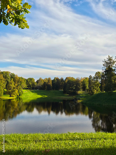 Fotografie Rolling green meadows by a mirror-like pond: English landscape park in September