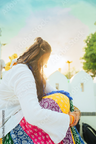 Portrait of a young Indian woman in traditional dress standing at an ancient temple in India, with carved stone pillars softly blurred in the background.