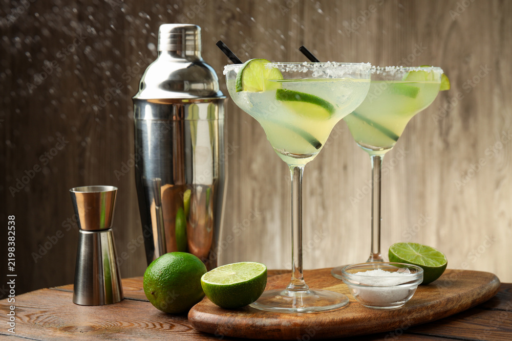 Obraz premium Delicious margarita cocktail in glasses, fresh fruits, salt, shaker and jigger on wooden table