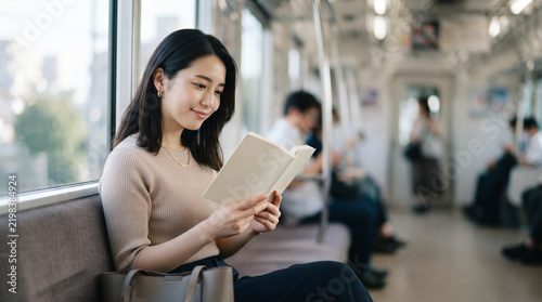 通勤電車の中で本を読む笑顔の若い女性