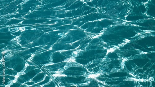 Clear turquoise water surface with sunlight reflections and ripple wave patterns creating aquatic texture