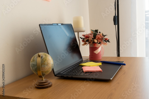 Modern home office desk with open laptop, colorful sticky notes, pen, globe and floral decor. Concept of remote work, online learning, global business, planning and creative productivity.