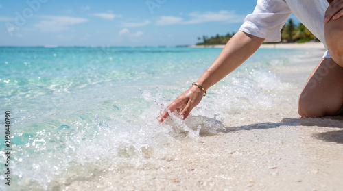Tropical Paradise Touch: A person's hand gently touches the crystal-clear turquoise water lapping onto a pristine white sand beach.