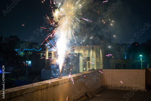 Colorful Diwali flowerpot fireworks bursting on a rooftop at night, with brightly decorated houses creating a festive Indian Festival of Lights atmosphere in India