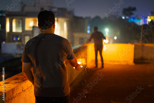 Man holding a firework sparkler while another in the distance lights up fireworks a common sight on the hindu festival of diwali in India