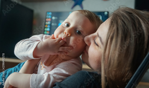 Fotografie Tender mother kissing her cute baby's cheek at home, expressing pure maternal love, care, and warmth