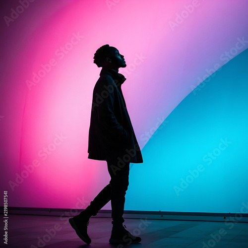 A striking silhouette stands against a vibrant neon pink and blue light gradient.