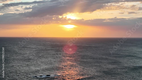 A sunset is seen over the ocean. The sky has clouds and colors as the sun sets. Waves gently move in the water.