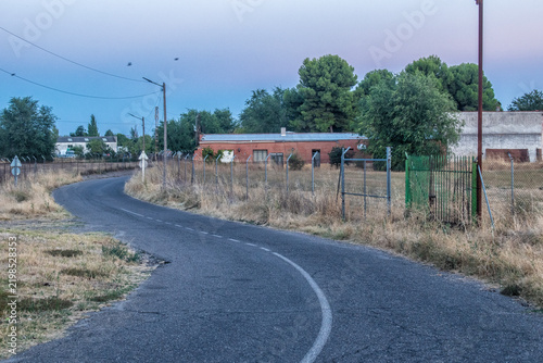 Obraz na plátně Rural road curving past buildings at sunset.