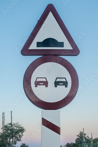 Two traffic signs on a post: no overtaking and speed bump warning.