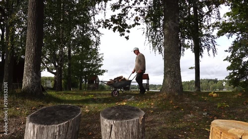 Stockholm, Sweden A man walks with a wheelbarrow of chopped wood in a yard. 