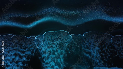 深い夜の海岸で暗い砂浜へ寄せる波が無数の生物発光により鮮烈な青色へ輝く