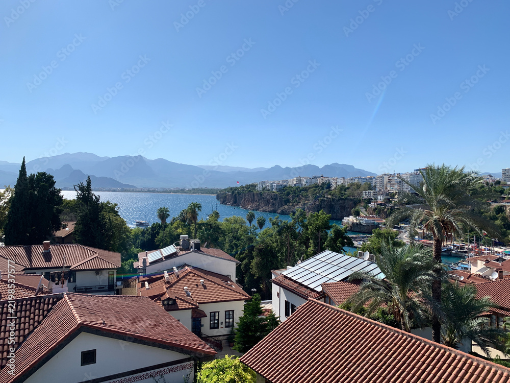 Obraz premium Panoramic view of the sea, mountains, and red-tiled roofs of Antalya’s historic old town, Turkey. Yenikapı and Kaleiçi districts. Roofs with solar panels.