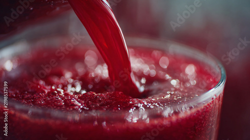 Fresh beet juice pouring into a glass with bubbles on the surface.