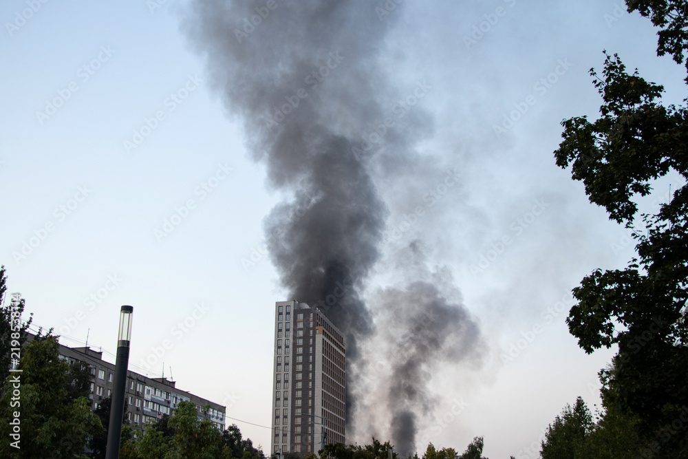 Obraz premium Thick black smoke rises from the top of an apartment building after a drone attack in Ukraine. The concept of fire, missile attack, drone raid