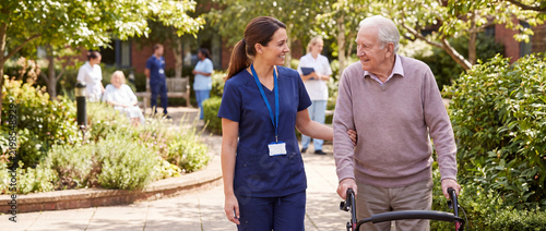 Nurse Assisting Senior Man with Walking Frame in Care Home Garden