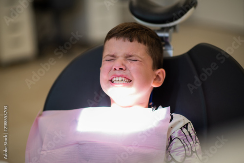 Scared little boy crying in a dental chair during treatment. Child experiencing fear and dental phobia at a pediatric dentist appointment, squeezing eyes shut.