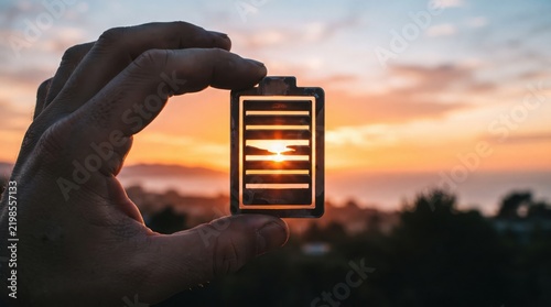 Hand holding a battery with a sunset glow symbolizing energy depletion and power