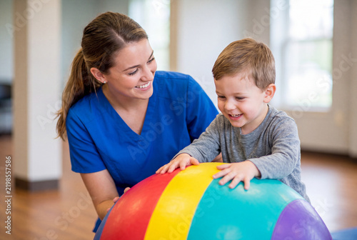 Pediatric Physical Therapist Helping Happy Toddler Boy with Colorful Exercise Ball and Sensory Exercises