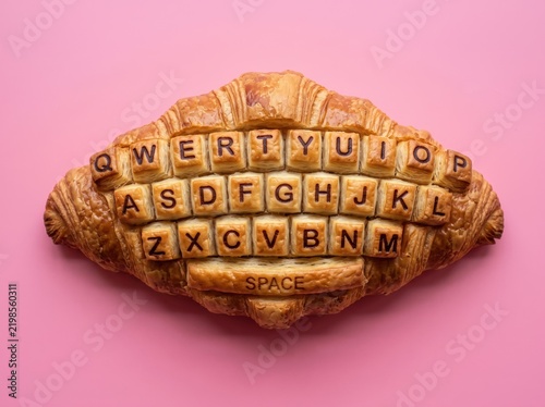 Croissant shaped computer keyboard on pink background