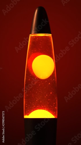 Glowing Orange Lava Lamp with Floating Yellow Wax Bubbles Against Red Background, Retro Psychedelic Mood Lighting