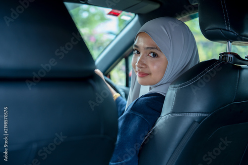 Young woman sitting on a driver's seat in the car and looking at camera over the shoulder