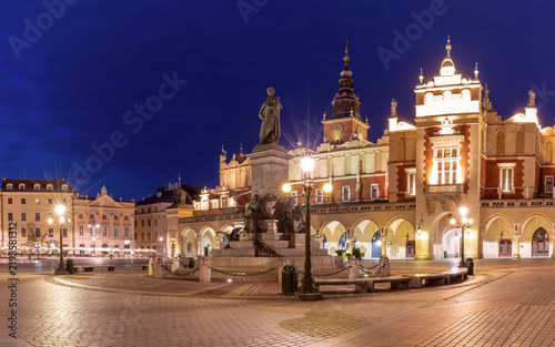 Illuminated Cloth Hall and Adam Mickiewicz Monument on Main Market Square in Krakow, Poland, during blue hour.