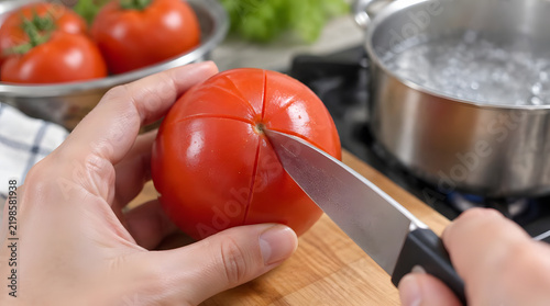 Scoring a fresh red tomato with a sharp knife before blanching in boiling water.