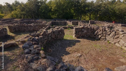 Ancient stone walls of the Castro de Romariz archaeological site standing amidst a sunlit Portuguese forest.