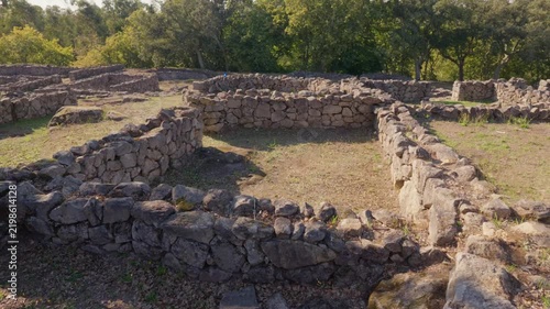 Ancient stone walls of the Castro de Romariz archaeological site standing amidst a sunlit Portuguese forest.