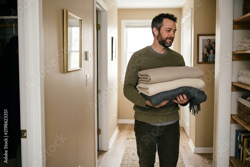 Man carrying a stack of neatly folded warm blankets down a home hallway