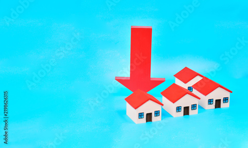 A downward arrow positioned behind miniature houses represents falling property prices and a weakening housing market.

