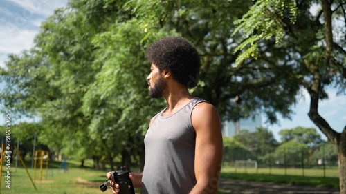 African American man with afro hair drinking water from metal bottle resting after workout session in sunny urban park daytime