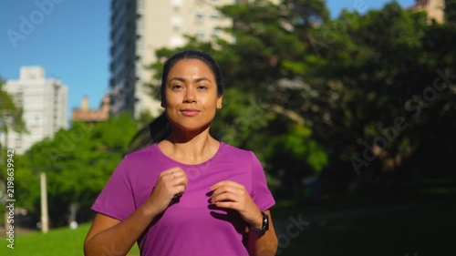 Woman, running and slow motion in park with fitness, cardio or active lifestyle outdoor. Front view, athlete or runner with ponytail, smart watch and endurance training in city.